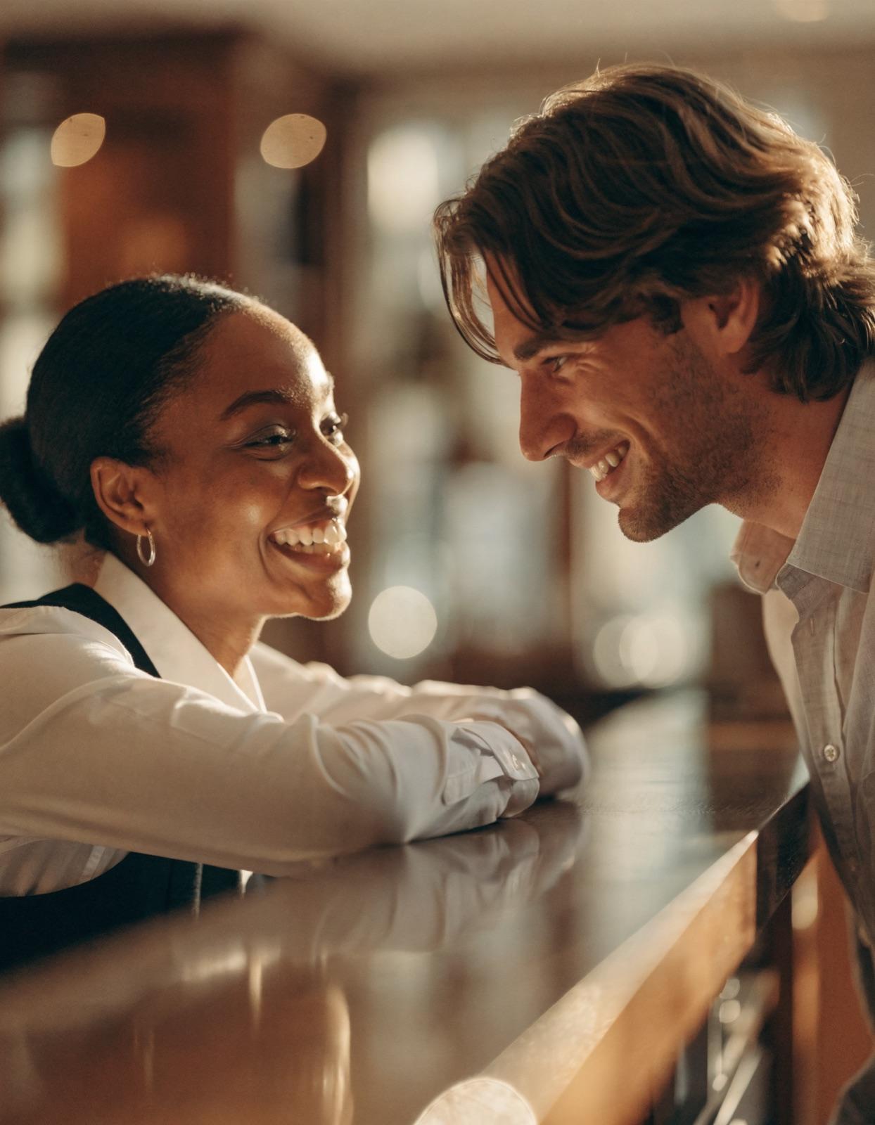 A hotel staff member and a guest smiling at each other across a counter