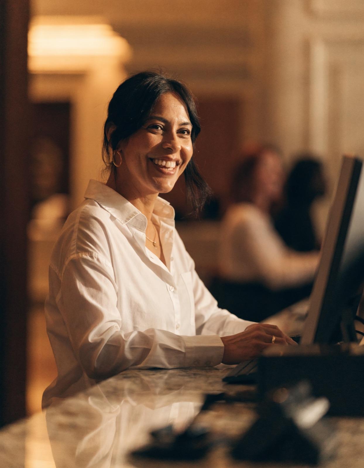 A hotel front desk receptionist smiling behind the reception counter