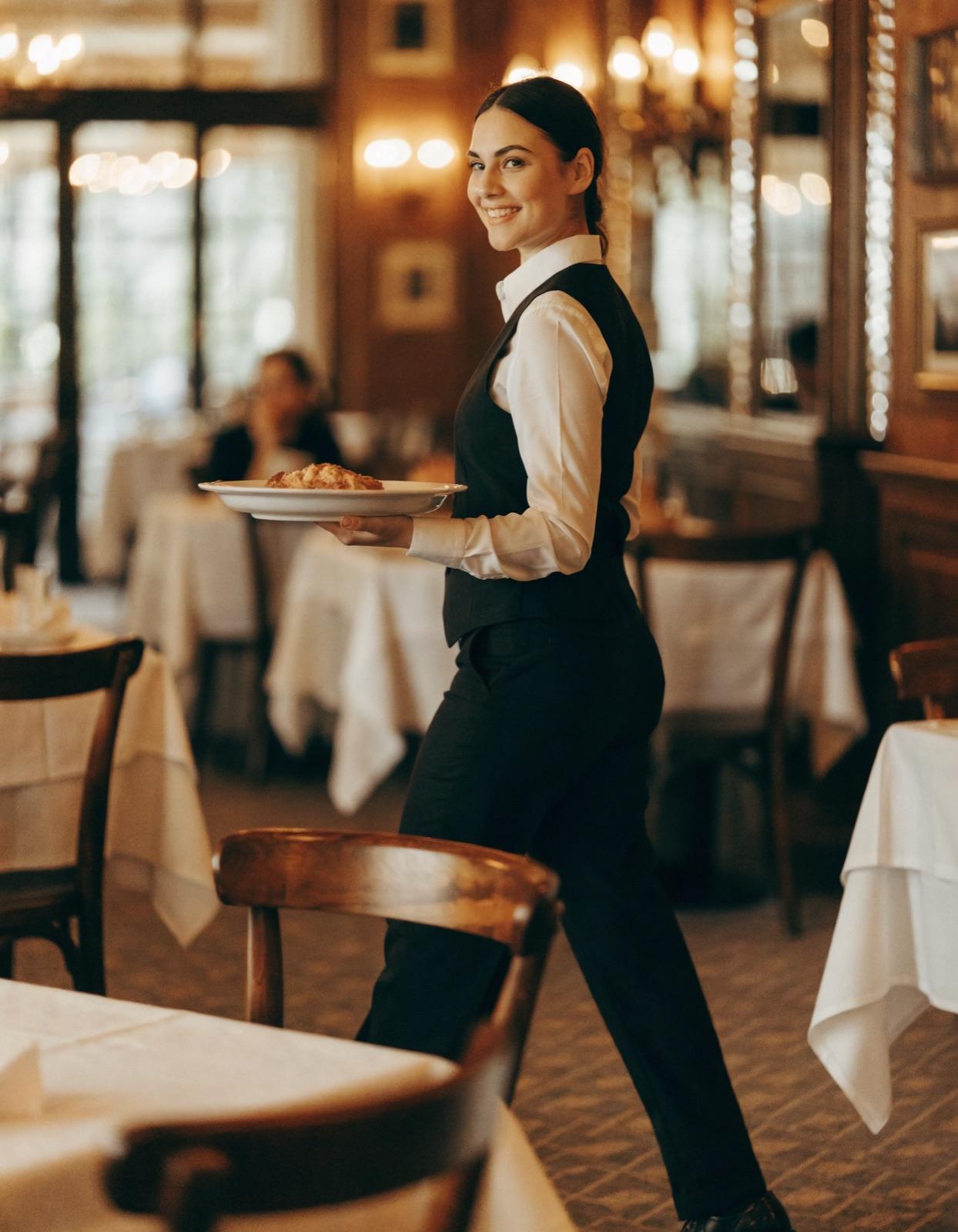 A hotel restaurant server carrying plates to a table