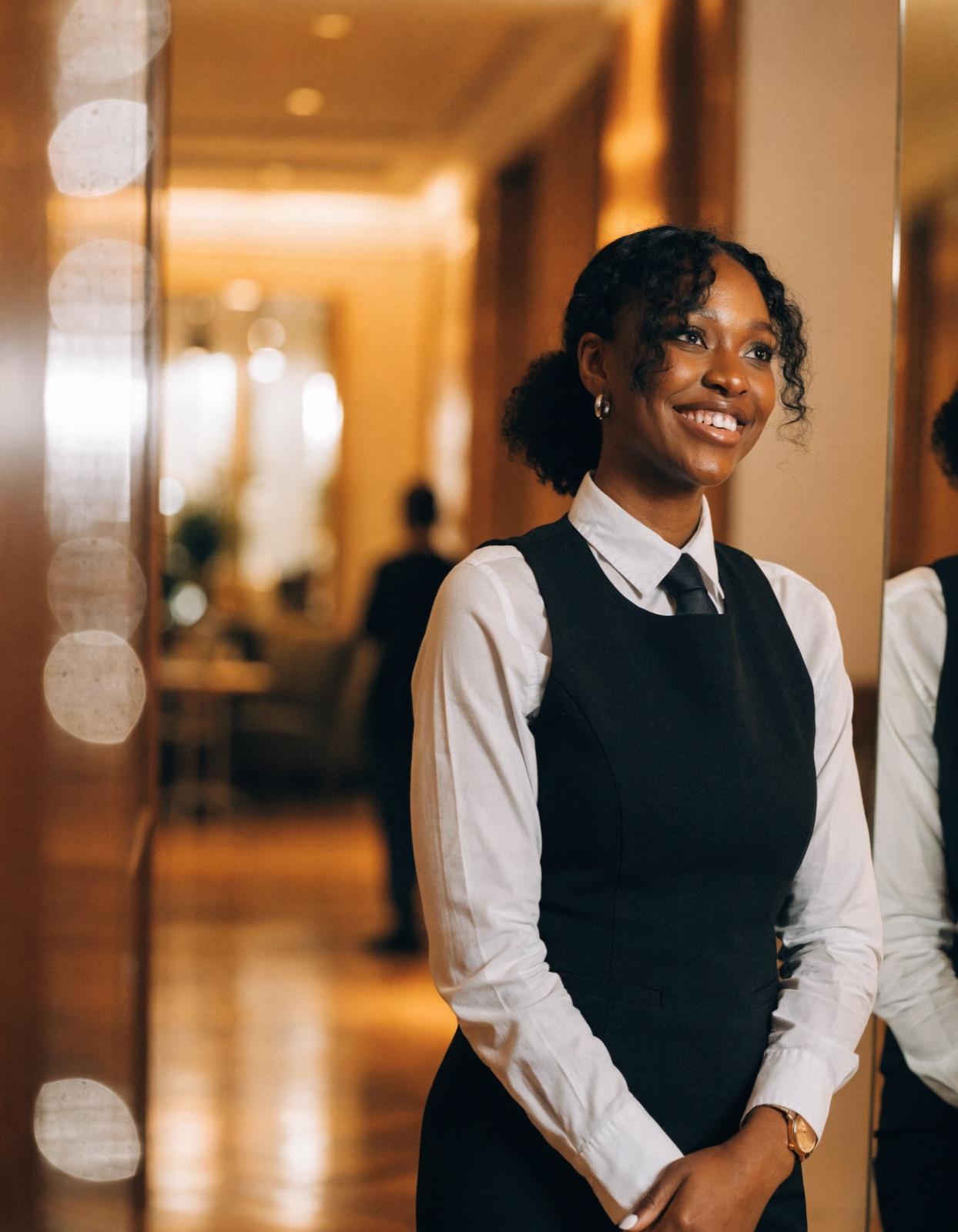 A smiling hotel staff member in uniform standing in a hotel corridor